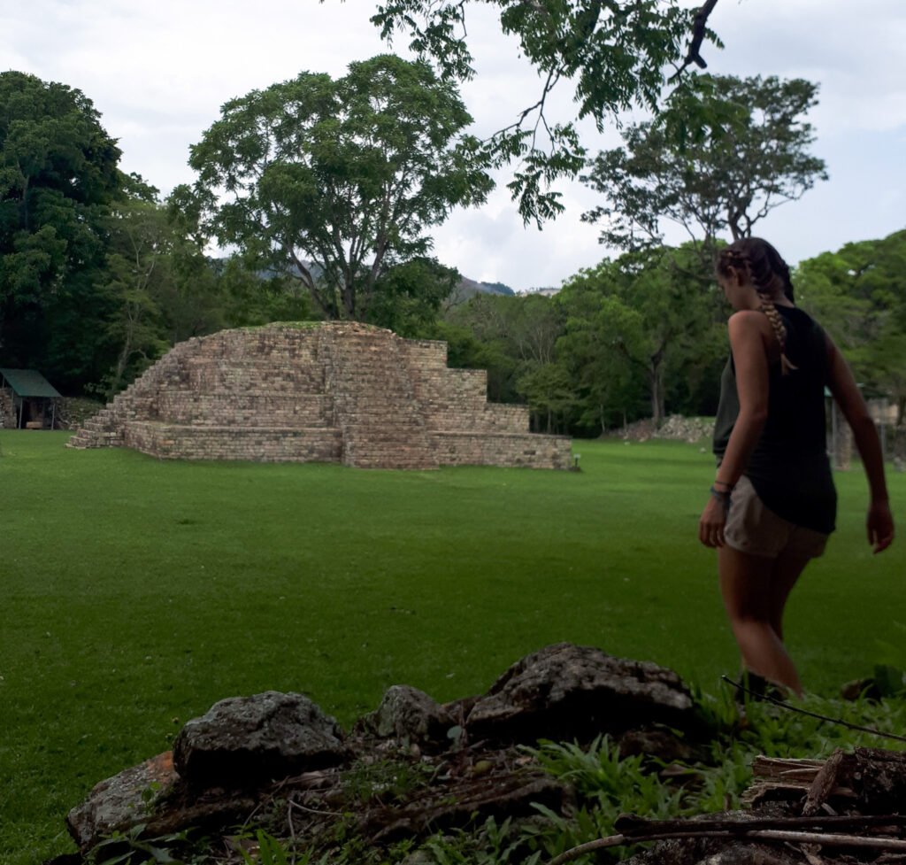 Foto das ruínas de Copán (Honduras) com uma mulher branca de costas com duas tranças