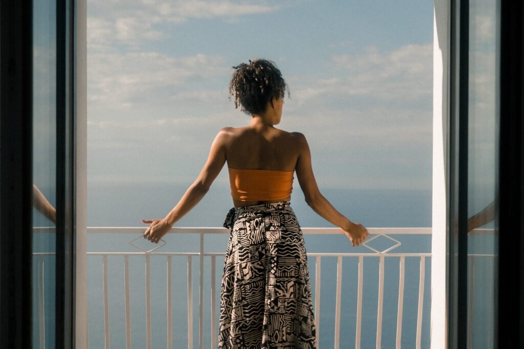 Mulher num balcão de costas observando o mar no horizonte